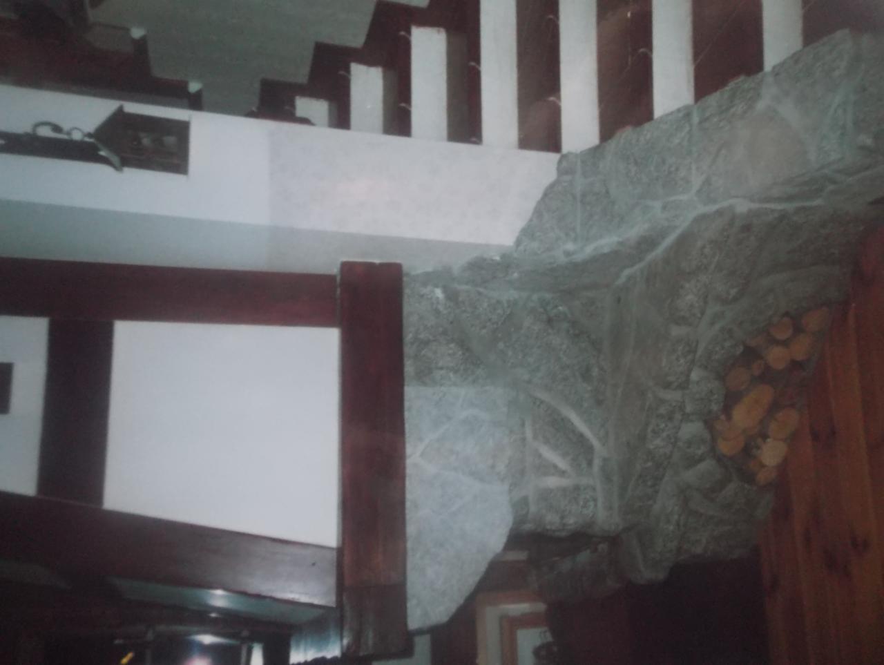 Fragment wnętrza z dekoracyjnym obłożeniem kamiennym ściany, drewnianymi elementami konstrukcyjnymi i schodami w tle.