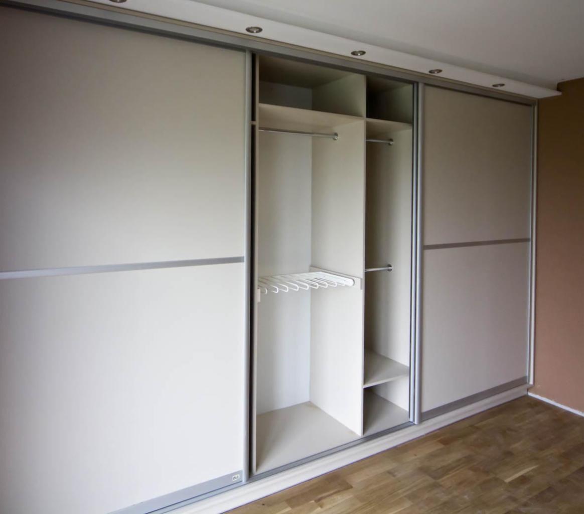 Wnętrze szafy wnękowej z przesuwnymi drzwiami w odcieniach beżu i szarości, widoczne półki i drążki na ubrania, drewniana podłoga.