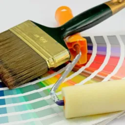 Szeroki pędzel malarski, wałek i paleta kolorów z próbkami odcieni, ułożone na białym tle.