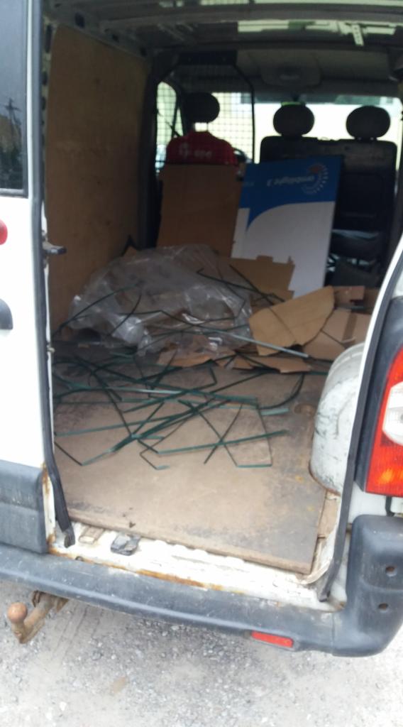 Wnętrze brudnego, białego busa wypełnione kartonami, folią i zielonymi elementami konstrukcyjnymi. Widoczne ślady rdzy na karoserii.