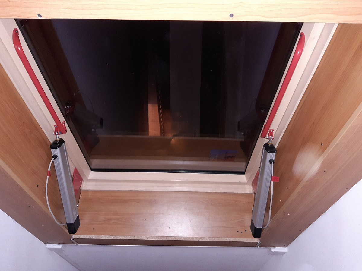 Okna dachowe z automatycznym systemem otwierania, widoczne siłowniki i czerwone elementy mocujące.