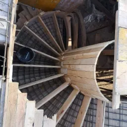 Konstrukcja szalunku spiralnych schodów z betonu z widocznym zbrojeniem i drewnianymi elementami podtrzymującymi, widok z góry.