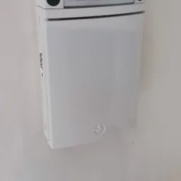 Biały panel sterowania systemu alarmowego zamontowany na ścianie, widoczne dwa czujniki i etykieta informacyjna na górze.