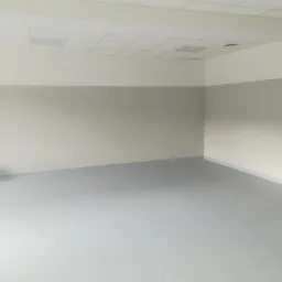 Pomalowane na szaro i biało puste pomieszczenie biurowe z podwieszanym sufitem rastrowym i szarą podłogą.