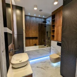 Nowoczesna łazienka w Rzeszowie z podświetleniem LED pod wanną i toaletą, marmurowe płytki na podłodze i ścianach, drewniane akcenty oraz umywalka nablatowa.