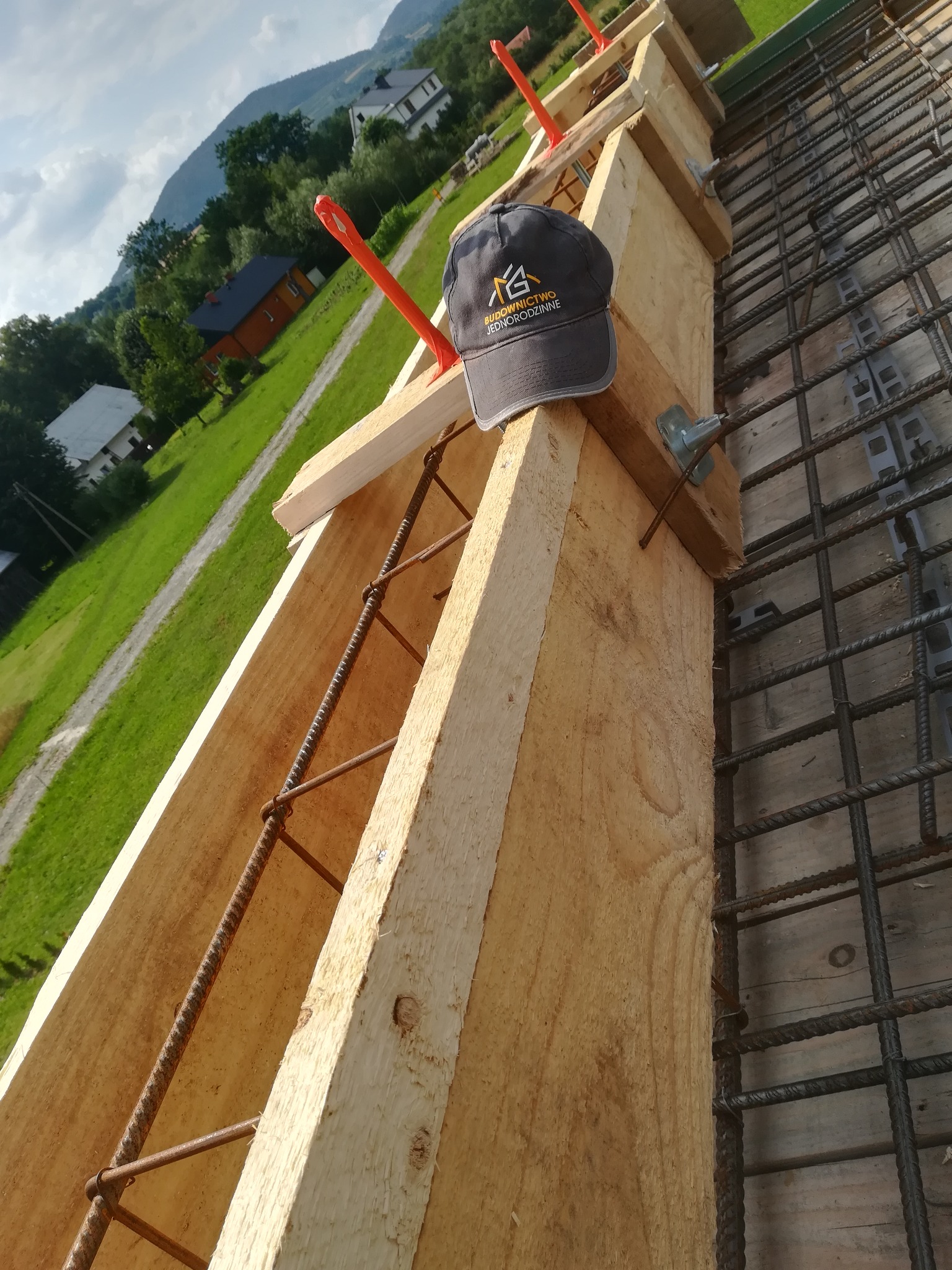 Zbrojenie szalunku fundamentu z widoczną czapką firmową na tle górskiego krajobrazu.