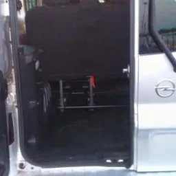 Wnętrze srebrnego Opla Vivaro z otwartymi drzwiami, widoczne zamontowane szyny do mocowania foteli lub wózków inwalidzkich.