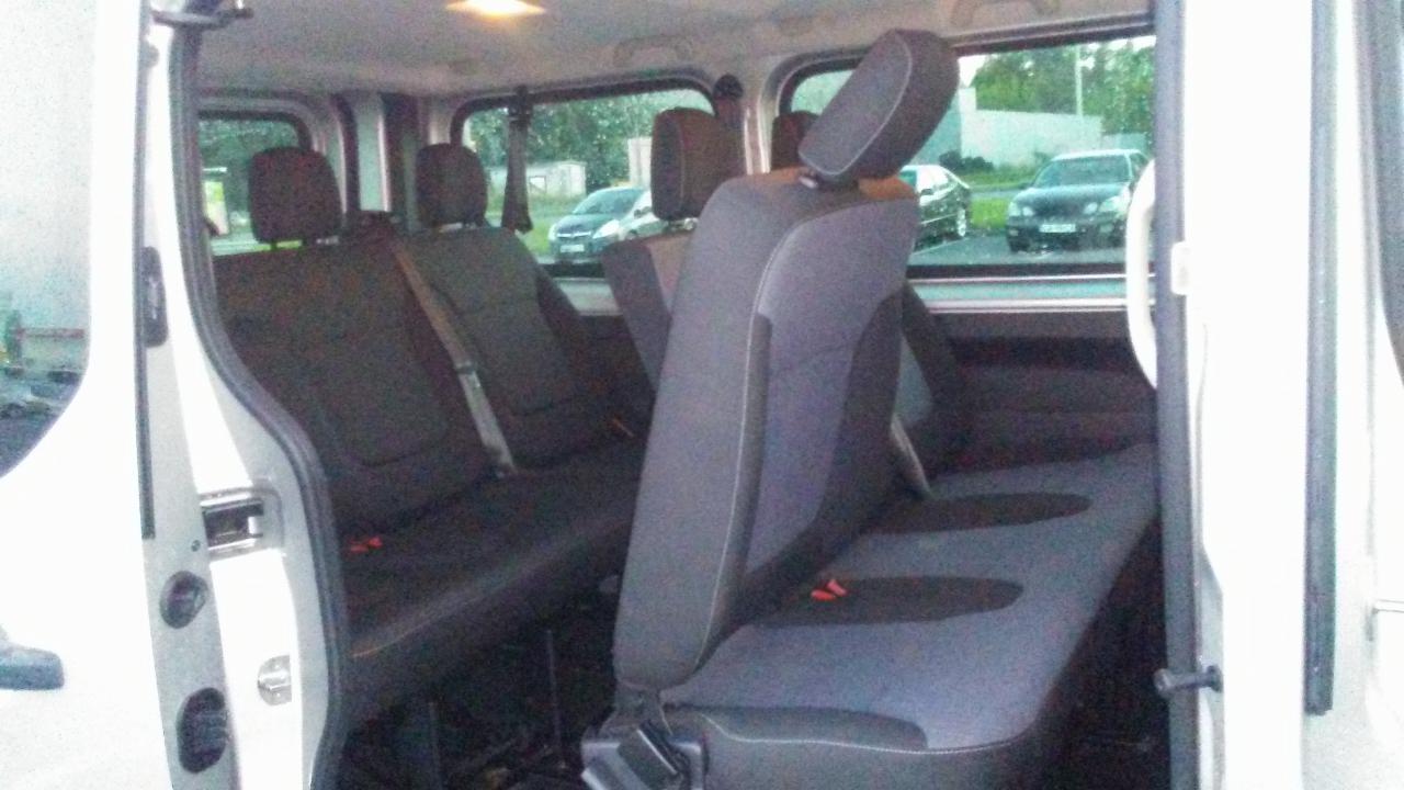 Wnętrze busa z ciemnymi fotelami widoczne przez otwarte drzwi w Łodzi, zarys samochodów w tle za oknem.