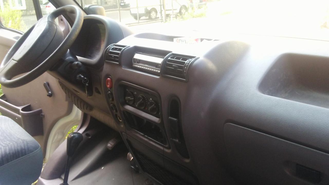 Wnętrze kabiny busa z widoczną deską rozdzielczą, kierownicą i dźwignią zmiany biegów, z zewnątrz widoczny fragment innego pojazdu.