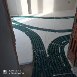 Montaż zielonych rur ogrzewania podłogowego na izolacji termicznej w Białymstoku, widoczne mocowania i pianka uszczelniająca.