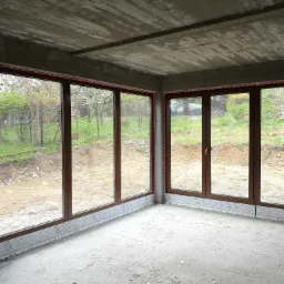 Surowy stan wnętrza z dużymi, brązowymi oknami z widokiem na ogród, widoczne pianki montażowe i nieotynkowane ściany.