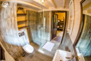 Wnętrze łazienki w stylu rustykalnym z kabiną prysznicową, drewnianymi elementami i umywalką, uchwycone szerokokątnym obiektywem.