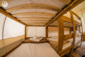 Wnętrze namiotu glampingowego z drewnianą konstrukcją łóżka piętrowego, białą pościelą i ręcznikami, widok z dołu na sufit namiotu.