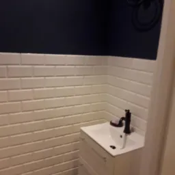 Nowoczesna łazienka z białymi płytkami typu metro, ciemnogranatową ścianą, białą szafką pod umywalką i dekoracyjną podłogą w stylu retro.