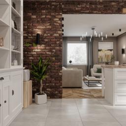 Osky Justyna Knapek - Nowoczesne wnętrze z ceglaną ścianą, białymi meblami i otwartym planem salonu, oświetlone designerskimi lampami.