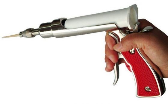 Pistolet do iniekcji żelowej z czerwoną rękojeścią, trzymany w dłoni, z widoczną końcówką aplikatora. Narzędzie do zwalczania szkodników w trudno dostępnych miejscach.