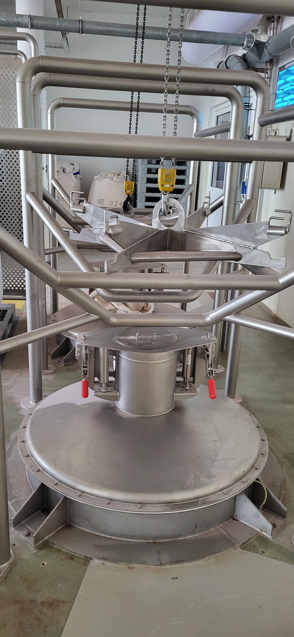 Metalowa konstrukcja z rur i blach, prawdopodobnie element linii produkcyjnej, z zawiesiami łańcuchowymi i elementami mocującymi. Widoczne spawane łączenia.