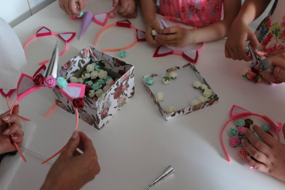 Dzieci tworzą ozdobne opaski z uszami i rogiem jednorożca, wykorzystując pudełka pełne małych, kolorowych kwiatków.
