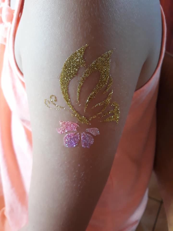 Złoty brokatowy motyl i różowy brokatowy kwiat na ramieniu dziecka, tymczasowy tatuaż.