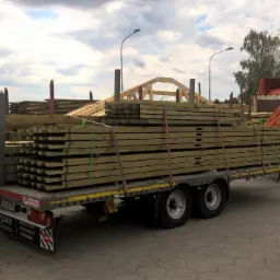 Transport impregnowanej tarcicy budowlanej oraz elementów więźby dachowej na przyczepie w Odolanowie, z widocznym żurawiem samochodowym.