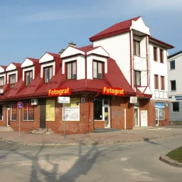 Budynek fotografa z czerwonym dachem i szyldami reklamowymi, widok z ulicy w słoneczny dzień.