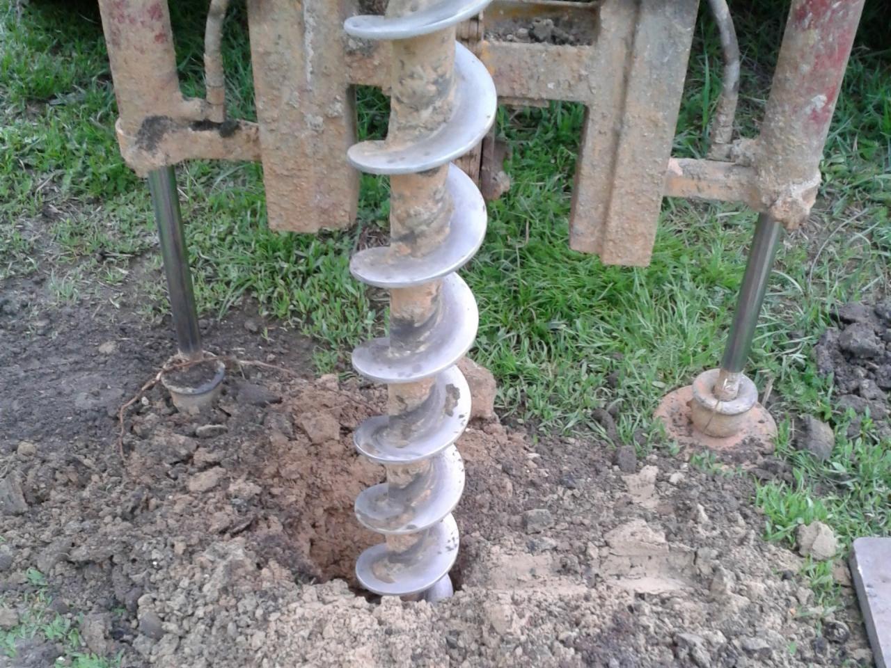 Wiertnica świdrowa zagłębiająca się w ziemię, widoczna spirala wiertła i fragment mechanizmu w tle.