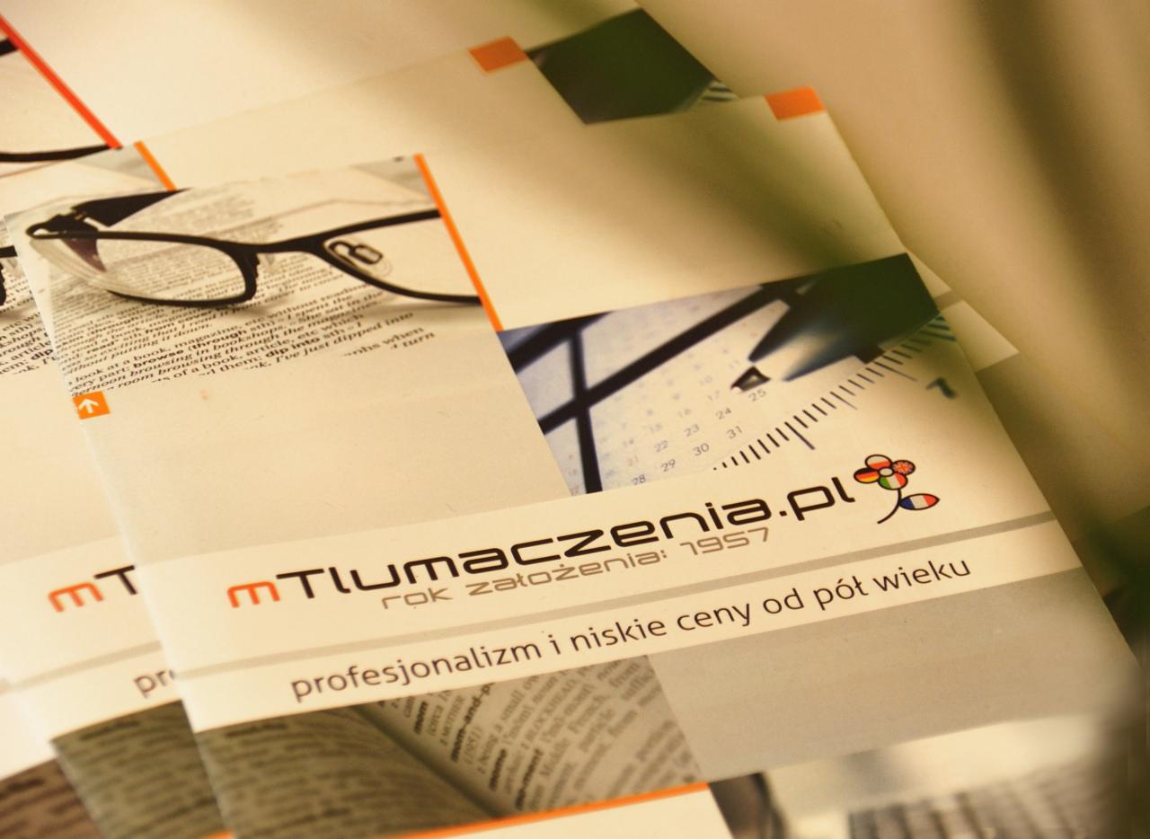 Stos ulotek reklamowych firmy tłumaczeniowej z hasłem 'profesjonalizm i niskie ceny od pół wieku', logo z domeną tlumaczenia.pl, kalendarz i okulary na tle tekstu.