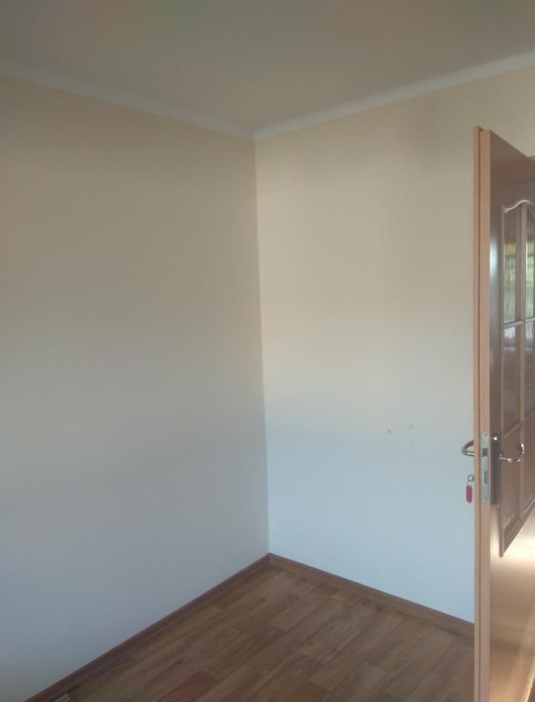 Pomieszczenie po malowaniu ścian na jasny odcień, widoczna drewnopodobna podłoga, biała listwa przypodłogowa i fragment otwartych drzwi z klamką