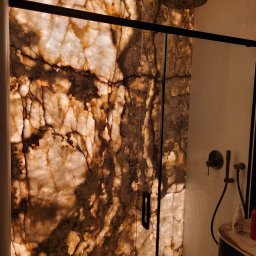 R&S PERFECT. WYKOŃCZENIA WNĘTRZ RYSZARD HAWRYLUK - Podświetlana ściana z onyksu w kabinie prysznicowej z czarną armaturą i szklanymi drzwiami.