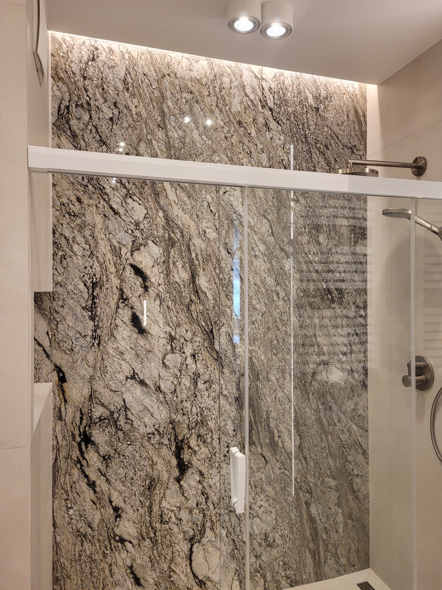 Wykończona kabina prysznicowa z marmurową ścianą w Tczewie. Szklane drzwi przesuwne, oświetlenie LED i nowoczesna armatura. Elegancki design łazienki.