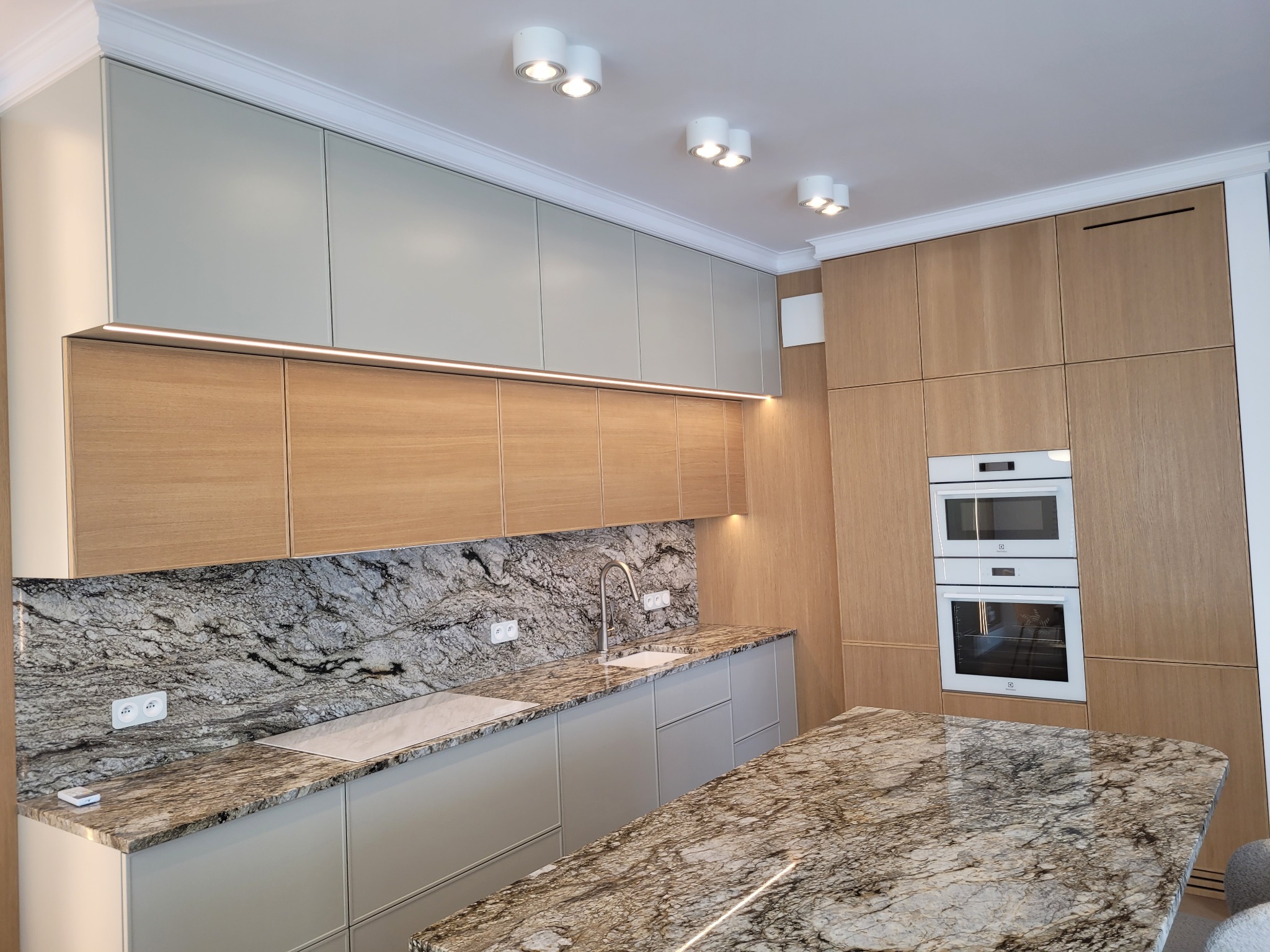 Nowoczesna kuchnia z marmurowym blatem i drewnianymi szafkami, oświetleniem LED podszafkowym i białymi sprzętami AGD. Widok na wyspę kuchenną z blatem z marmuru.