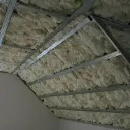 Skośny strych z widoczną konstrukcją metalową i wypełnieniem z wełny mineralnej, okno w ścianie szczytowej, widok z dołu.