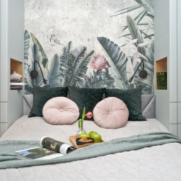 Lucarna Meble - Jasnoszara sypialnia z łóżkiem w zabudowie szafy, tapeta z motywem tropikalnych liści, okrągłe różowe poduszki i śniadanie na tacy.