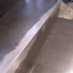 TOTAL METAL - Szlifowana powierzchnia metalowa z widocznymi śladami obróbki i krawędzią pod kątem.