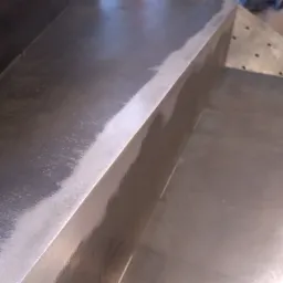 Szlifowana powierzchnia metalowa z widocznymi śladami obróbki i krawędzią pod kątem.