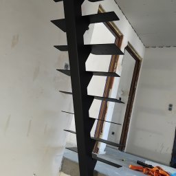 TOTAL METAL - Surowe, metalowe schody policzkowe w trakcie montażu, z widocznymi uchwytami stopni i elementami mocującymi, na tle niewykończonego wnętrza z widocznymi przewodami elektrycznymi i narzędziami.