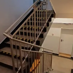 Wewnętrzne schody betonowe z metalową balustradą, zabezpieczone taśmami ostrzegawczymi na krawędziach stopni, widok z góry.