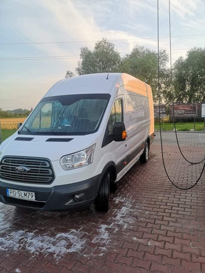 Biały Ford Transit z polską tablicą rejestracyjną PO 5LM79, stojący na czerwonej kostce brukowej po umyciu, z widocznymi śladami wody.