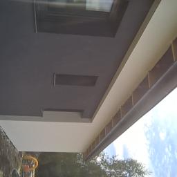 Tomasz Woszczyk - Elewacja domu jednorodzinnego z widocznym oknem, świeżo pomalowana na szaro i biało, z zamontowaną rynną, widok z dołu.