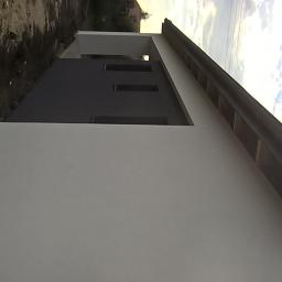 Tomasz Woszczyk - Świeżo otynkowana ściana zewnętrzna domu z widocznymi otworami okiennymi, częściowo pomalowana na szaro, z widocznym fragmentem dachu i niebem w tle.