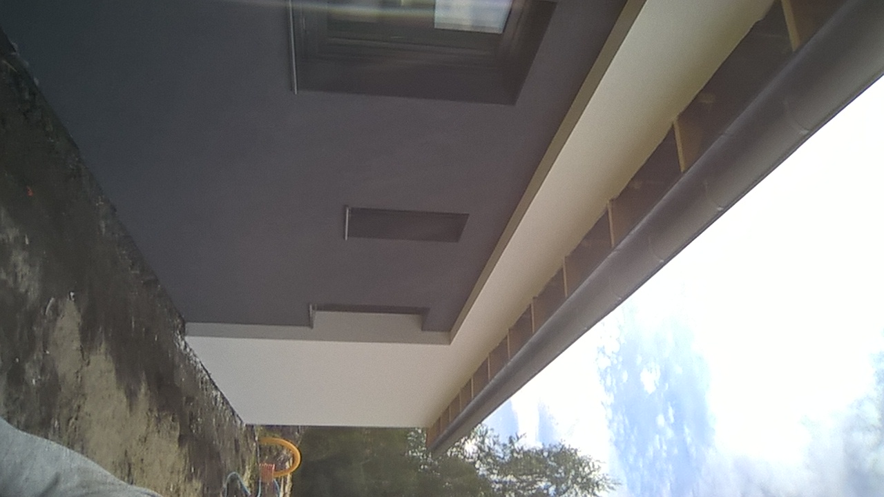 Elewacja domu jednorodzinnego z widocznym oknem, świeżo pomalowana na szaro i biało, z zamontowaną rynną, widok z dołu.