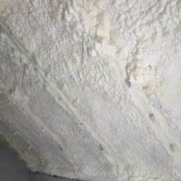 Świeżo nałożona, biała izolacja natryskowa w przestrzeni poddasza, widoczne drewniane elementy konstrukcyjne.