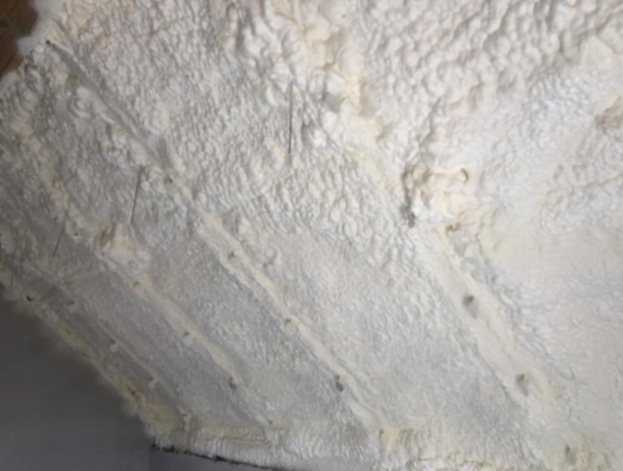 Świeżo nałożona, biała izolacja natryskowa w przestrzeni poddasza, widoczne drewniane elementy konstrukcyjne.