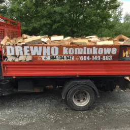 Ciężarówka z otwartą skrzynią załadowaną pociętymi kawałkami drewna, z reklamą firmy i numerami telefonów na burcie.