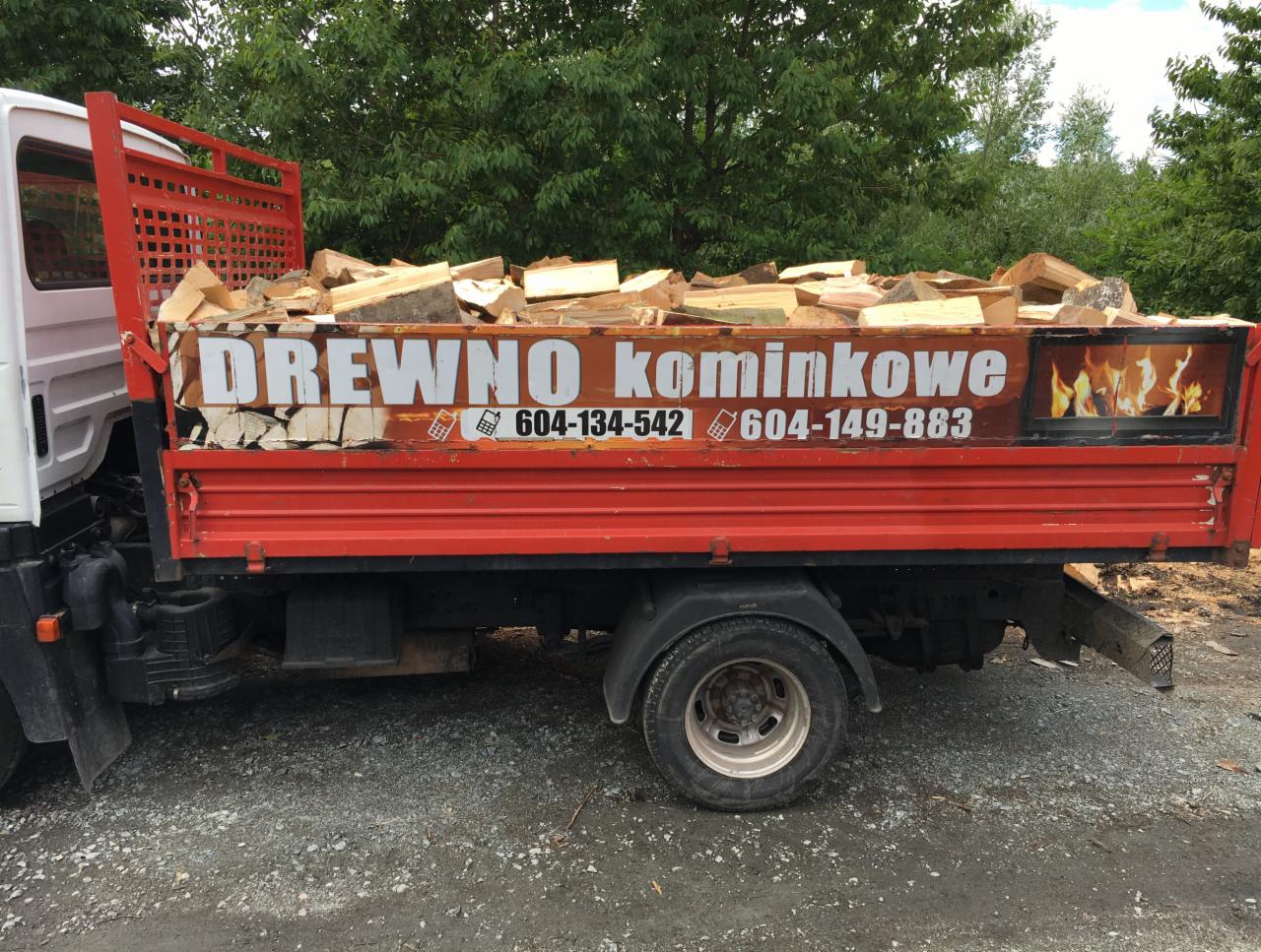 Ciężarówka z otwartą skrzynią załadowaną pociętymi kawałkami drewna, z reklamą firmy i numerami telefonów na burcie.