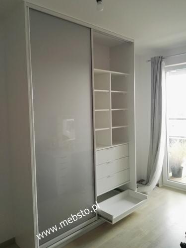 Biała szafa wnękowa z przesuwnymi drzwiami i wysuwaną szufladą w Luboniu, widok na półki i szuflady wewnątrz.