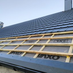 Usługi Blacharsko-Dekarskie Łukasz Siwkowski - Montaż czarnej dachówki na łatach w Działdowie, widoczny komin i pracownik na dachu.