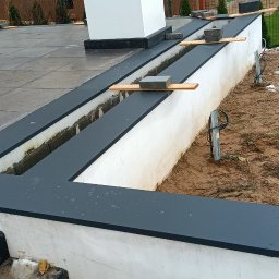 Usługi Blacharsko-Dekarskie Łukasz Siwkowski - Wykończony dach płaski z obróbkami blacharskimi w kolorze grafitowym, widoczne elementy mocujące i przygotowany teren wokół budynku.
