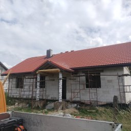 Usługi Blacharsko-Dekarskie Łukasz Siwkowski - Dom w trakcie budowy z nowym, czerwonym dachem z dachówki ceramicznej, widoczne rusztowania i elementy konstrukcyjne z drewna.