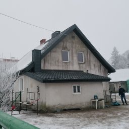 Usługi Blacharsko-Dekarskie Łukasz Siwkowski - Dom jednorodzinny z nowym, ciemnym dachem z dachówki ceramicznej w zimowej scenerii, widoczne rusztowanie, narzędzia i osoba w oddali.